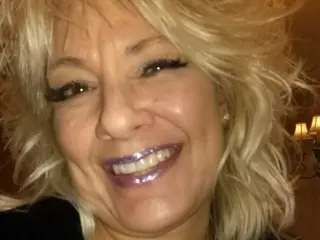 sexmittennjoytoy smiles with her blonde hair styled in soft waves, showing her face and shoulders against a warm background.