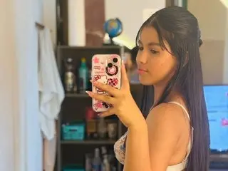smith_liam poses for a mirror selfie, showing her long dark hair and bare shoulders in a bright room.