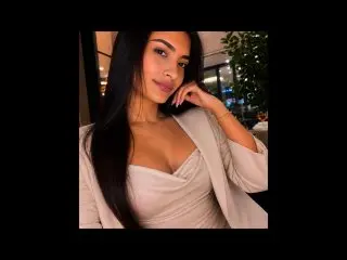 sofiascarlett poses with long dark hair, wearing a white wrap top that shows cleavage, looking directly at the camera.