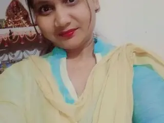 Smiling woman in a blue and yellow traditional Indian salwar kameez outfit in a home setting.
