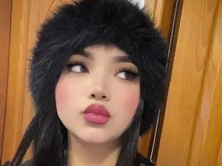 sweetgirlshot poses close-up with long dark hair and a thick black furry hat against a wooden door background.