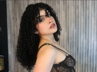 vaneblake — vaneblake poses with long curly dark hair wearing a black lace bra against a grey slatted wall.
