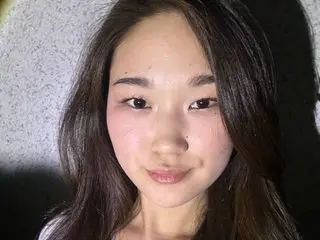 very_hot_japanese_girl poses for a close-up headshot, showing her long dark hair and clear skin against a dark background.