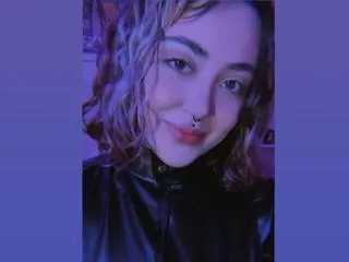 violet_smile poses with a slight smile, wearing a black leather top with her wavy hair falling over her shoulders.