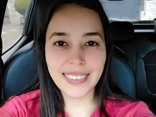 whites_and_black smiles while looking at the camera, showing her long dark hair and wearing a red top while sitting in a car seat.