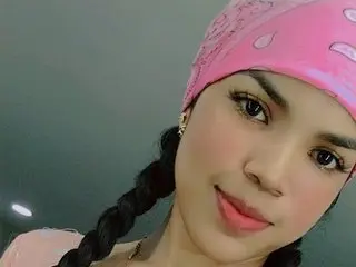 ximena_ruiz poses close-up with her dark hair in long braids and a pink patterned headwrap against a plain grey background.