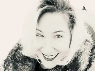 xxNATxxX smiles closely at the camera, showing her face and blonde hair while wearing a thick, dark fur collar.