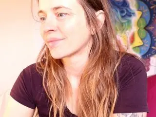 xxXxPixeyxXxx has long brown hair and a slight smile, wearing a black v-neck t-shirt in a bright indoor setting.
