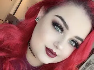 xxxKAYxxx has long red hair and dark eyes, wearing a dark top while looking directly at the camera.