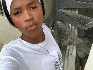 your_blackk poses close-up, wearing a white tank top and a white headband, looking directly at the camera with a neutral expression.