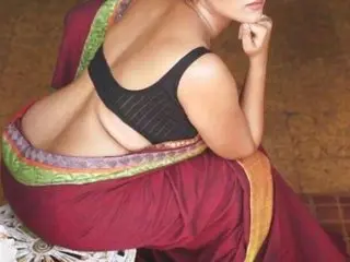 yourshnishaa poses with her back turned, showing her bare back and curves while wearing a red and gold traditional outfit.