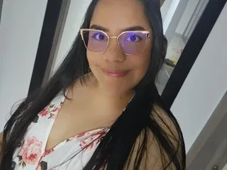 zoedeleon smiles in a white floral sundress and glasses while looking at the camera.