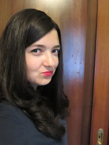 Smiling woman with long dark hair and red lipstick posing in front of a wooden door.