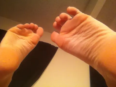 Close-up view of bare human feet resting against a neutral indoor background in soft lighting.