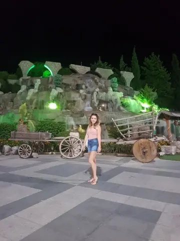Young woman in a pink top and denim shorts standing before a magical illuminated rock garden at night.