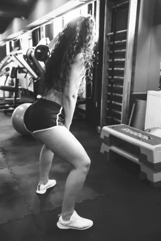 Fit woman in black athletic shorts performing squats in a gym setting, focused workout mood.