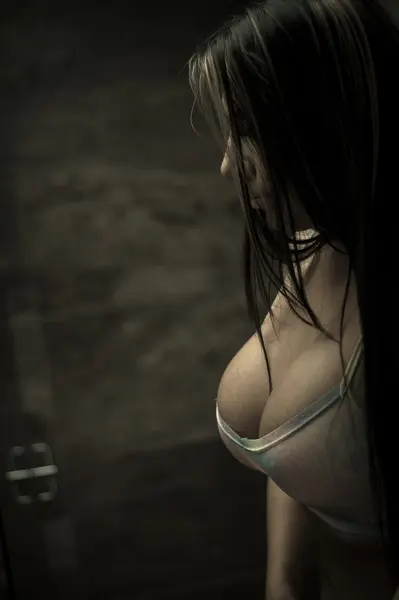BelleJolie poses in a dark bikini while standing on a wooden deck surrounded by a dense forest.