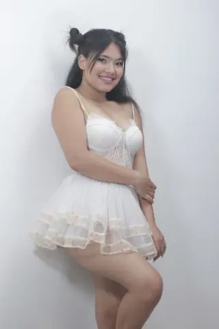 Smiling young woman in a white lace lingerie set posing against a plain white background.