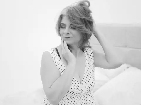 Thoughtful middle-aged woman in a polka dot sleeveless top relaxing in a bright, minimalist bedroom.
