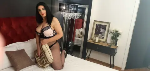 Woman in black lace lingerie and fishnet tights sitting on a bed in a moody, modern bedroom.