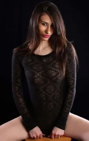 Young woman in a black lace long-sleeve bodysuit posing against a dark background with a moody aesthetic.