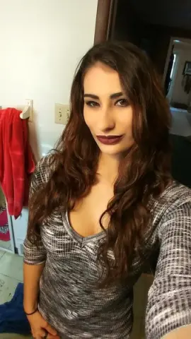 Young woman with long wavy hair wearing a grey textured v-neck top in a bright indoor setting.