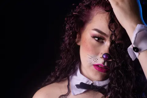 Woman in cat costume with whiskers and bow tie posing against a dark background with moody lighting.