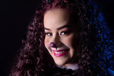 Smiling woman in cat costume makeup and curly hair posing for a playful dark themed portrait.