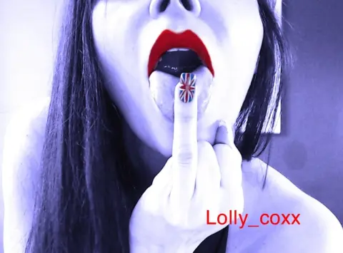 Lolly_coxx looks into the camera with red lipstick and her mouth open, holding her middle finger up to her tongue with a Union Jack nail design.