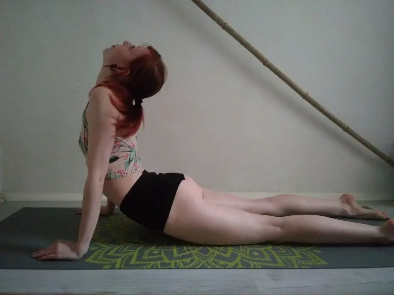 Redheaded woman in a lace camisole and gold jewelry posing with a soft, dreamy expression indoors.