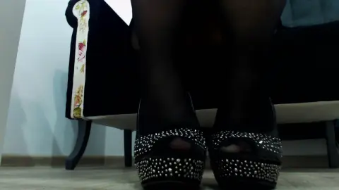 Close-up of elegant black studded peep-toe heels worn in a cozy indoor setting.