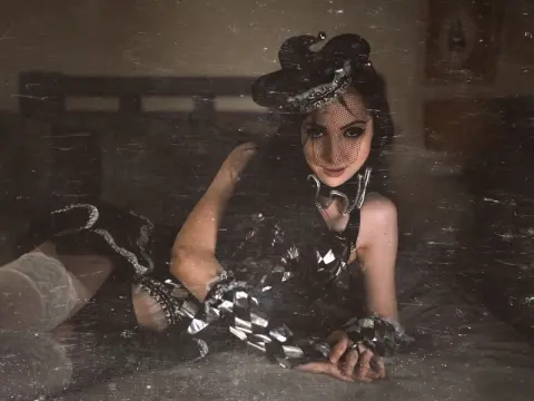 Elegant woman in black lace lingerie and veil reclining on a bed in a moody, vintage bedroom setting.
