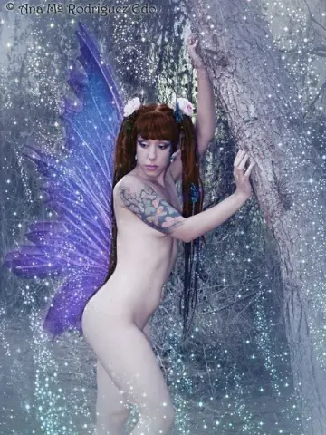 Sofi_Mora is a naked fairy with purple wings and red hair, posing nude against a tree in a magical forest.
