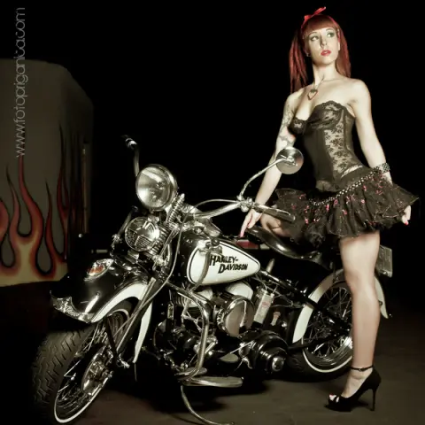 Sofi_Mora poses in a black lace corset and ruffled mini skirt while leaning against a Harley-Davidson motorcycle.