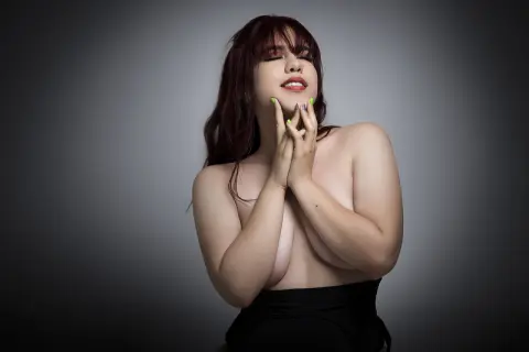 Beautiful woman with red hair posing gracefully in black clothing against a moody grey studio background.