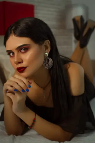 Glamorous woman with dark hair and red lipstick wearing large hoop earrings, relaxing in a cozy indoor setting.