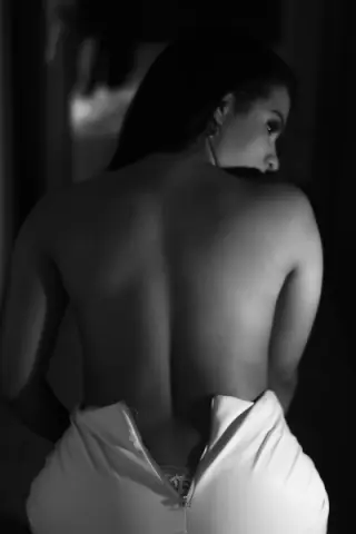 Elegant woman in a white backless evening gown posing in a moody, cinematic black and white setting.