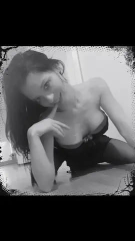 Smiling woman in black lingerie relaxing on a floor in a moody black and white portrait.