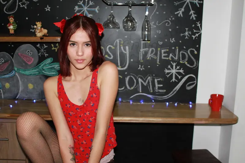 lexyRoss — Young woman in a red floral tank top and fishnet tights sitting by a chalkboard menu in a cozy cafe.