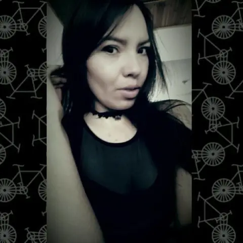 Young woman in a black top posing for a moody indoor selfie against a patterned background.